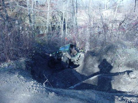 1992 Ford Bronco - A green off-road vehicle navigates a steep dirt incline surrounded by bare trees.
