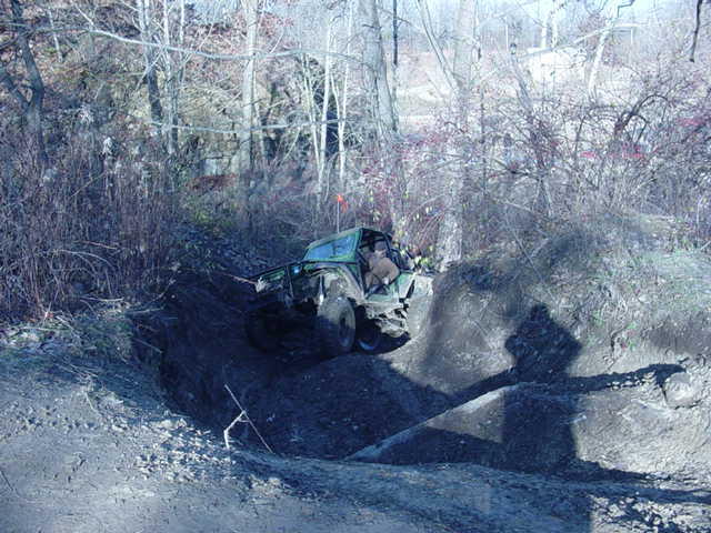 Green off-road vehicle with exposed roll cage climbing a dirt embankment