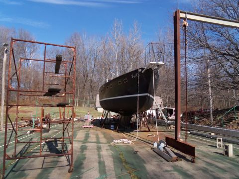 1989 Ford Bronco - A black sailboat named Faith rests on stands in an outdoor yard, surrounded by scaffolding and equipment.