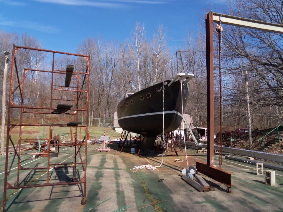 Black sailboat named Faith on stands, with scaffolding and a hoist