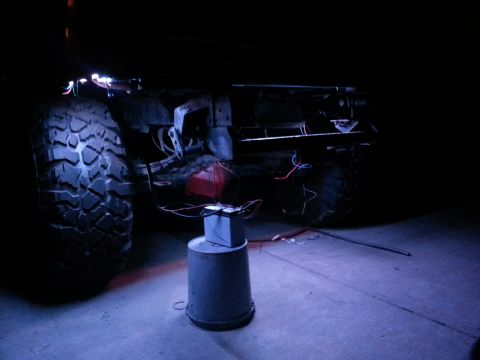 1978 Ford Bronco - The underside of a vehicle is lit up with blue rock lights, showing exposed wiring and suspension components.