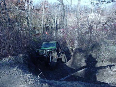 1992 Ford Bronco - An off-road vehicle navigates a challenging muddy terrain surrounded by dense trees.