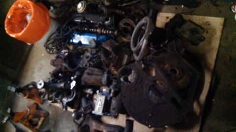 1977 Ford F-150 - Various engine components are scattered across a wooden surface, with an orange bucket nearby.