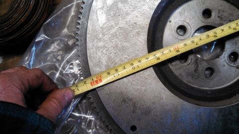 1977 Ford F-150 - A person is measuring a flywheel with a tape measure, showing its diameter and teeth.