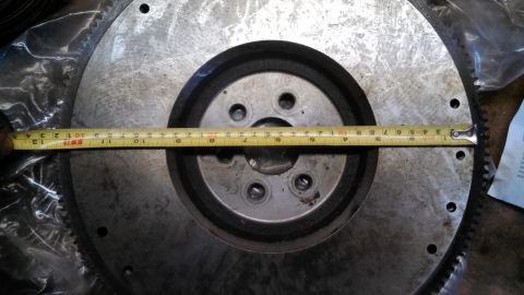 1977 Ford F-150 - A metal flywheel is measured with a tape measure, indicating its size.