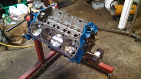 1977 Ford F-150 - A blue engine block with visible pistons is mounted on a red engine stand in a workshop setting.