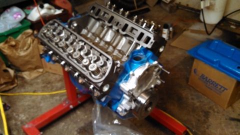 1977 Ford F-150 - Engine assembly on a stand, with a blue valve cover nearby. The registry claims it is a 1977 Ford F-150, but this is a part.