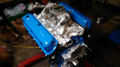 1977 Ford F-150 - A V8 engine assembly is shown with blue valve covers and a carburetor, resting on a red engine stand.
