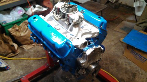 1977 Ford F-150 - A V8 engine with bright blue valve covers is mounted on a red engine stand in a workshop setting.