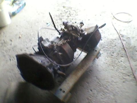 1977 Ford F-150 - Various engine and transmission parts are shown resting on a wooden support structure on a concrete floor.