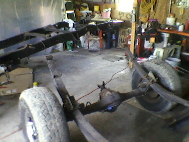 Truck frame with rear axle and leaf springs visible, in a garage setting