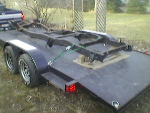 1977 Ford F-150 - A bare truck frame is secured with straps on a trailer, ready for transport.