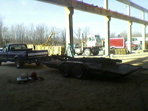 1977 Ford F-150 - A dark blue pickup truck from the early 1990s is towing a flatbed trailer under a large structure.