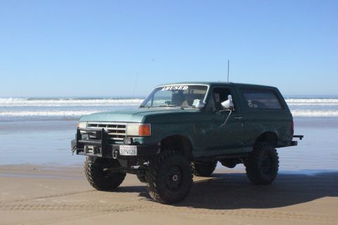 1991 Ford Bronco - A modified green Ford Bronco sits on a beach with the ocean in the background.