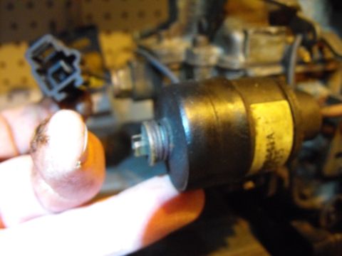 1983 Chrysler Fifth Avenue - A close-up view of a carburetor component being held by a hand, with a yellow label visible on the part.