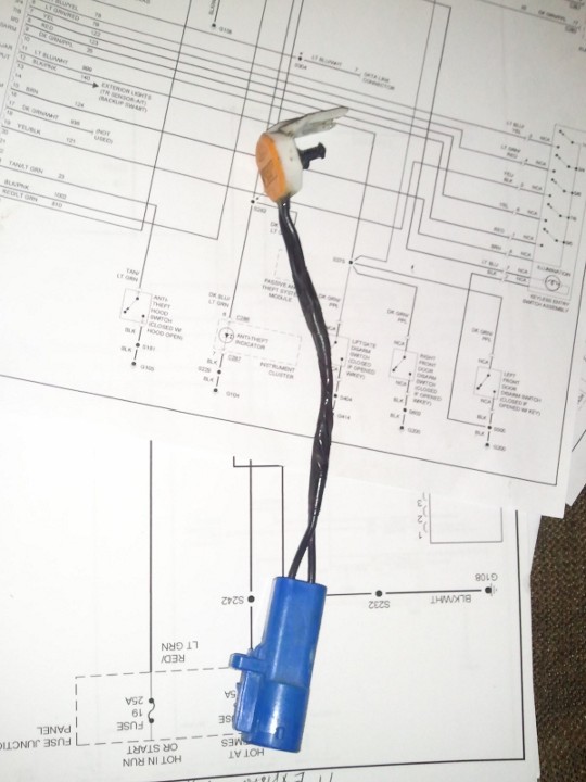 Wiring diagram printout with color-coded circuits and a connector pigtail laid on top