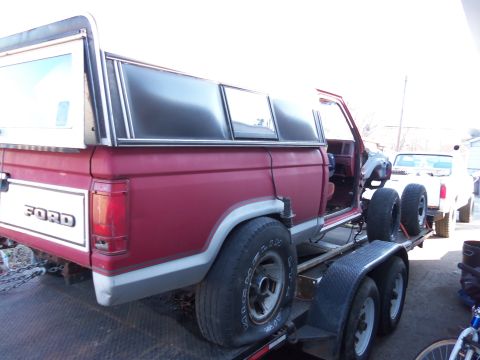 1987 Ford Ranger - A red 1987 Ford Ranger pickup truck with a white camper shell is loaded onto a trailer, with another white truck visible behind it.