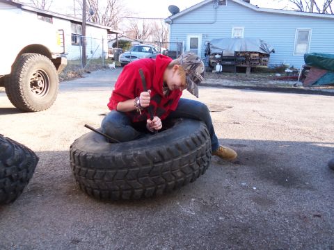 1987 Ford Ranger - Person working on a large tire with a tool, with another tire nearby.