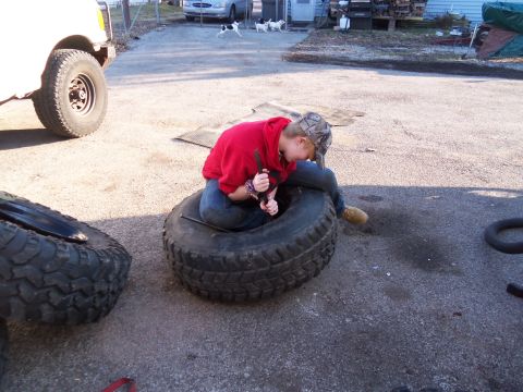 1987 Ford Ranger - A person works on a large tire in a yard with a truck and dogs present.