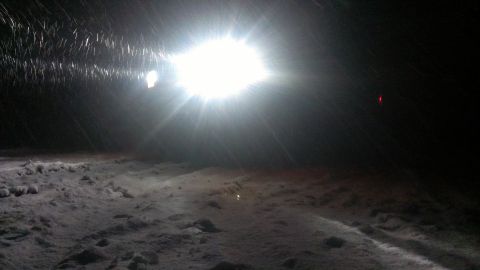 1995 Ford Bronco - Headlight illuminates a snowy scene at night with falling snow.