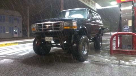 1995 Ford Bronco - Black Ford Bronco with large tires parked at a gas station during a rain storm.