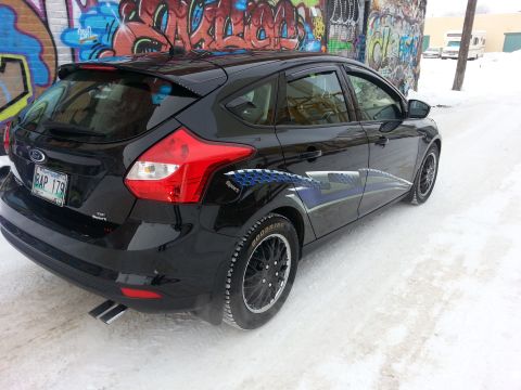 2012 Ford Focus - A black 2012 Ford Focus hatchback is parked on a snowy street with graffiti in the background.