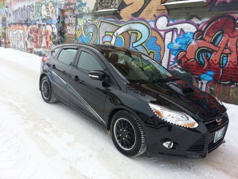 2012 Ford Focus - A black 2012 Ford Focus hatchback is parked on a snowy street in front of a graffiti-covered wall.