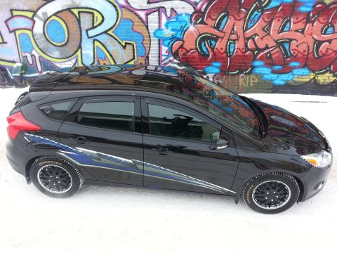 2012 Ford Focus - Black 2012 Ford Focus hatchback with racing stripes in front of a graffiti-covered wall.