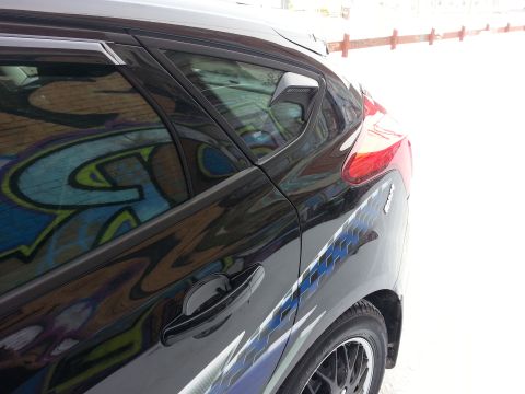 2012 Ford Focus - Rear side view of a black 2012 Ford Focus, showing a graffiti reflection in the window.