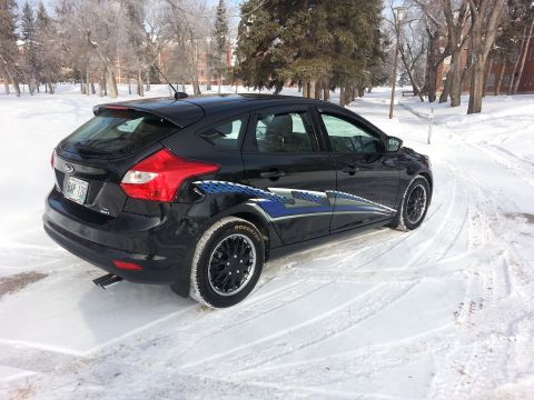 2012 Ford Focus - A black Ford Focus hatchback is parked on a snow-covered road with trees in the background.