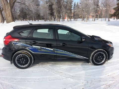 2012 Ford Focus - A black hatchback with custom racing stripes sits in a snowy landscape, showing its side profile and aftermarket wheels.