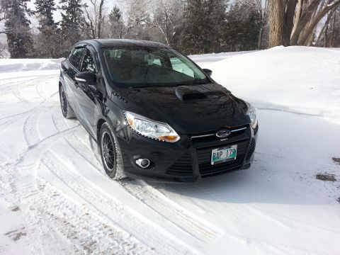 2012 Ford Focus - A black Ford Focus is parked on a snowy road with trees in the background.