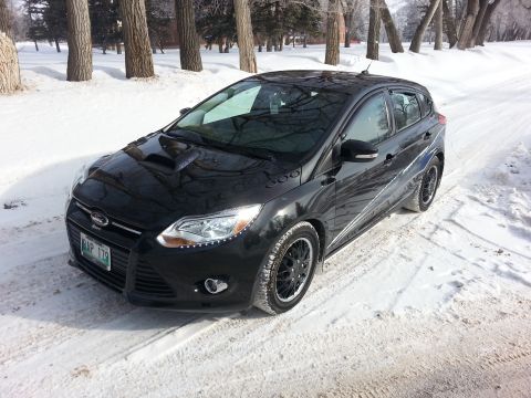 2012 Ford Focus - A black Ford Focus hatchback is parked on a snow-covered road with trees in the background.