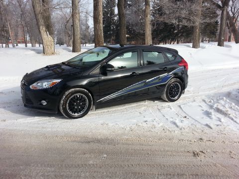 2012 Ford Focus - A black 2012 Ford Focus hatchback is parked on a snow-covered road with trees in the background.