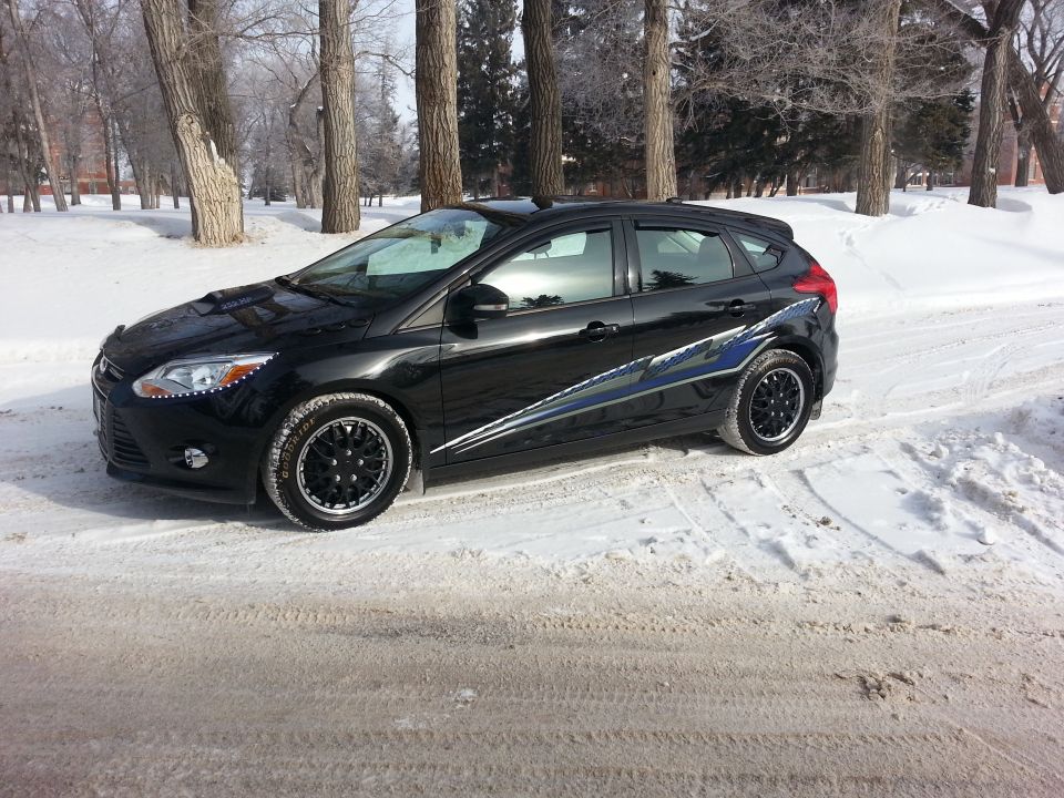 Black 2012 Ford Focus hatchback with blue and white side decals parked on a snowy road