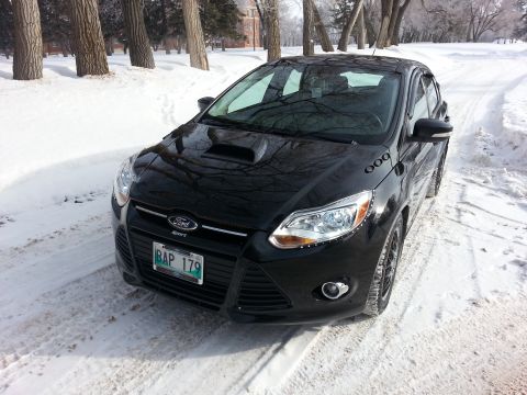 2012 Ford Focus - A black Ford Focus is parked on a snow-covered road, with trees lining the background.