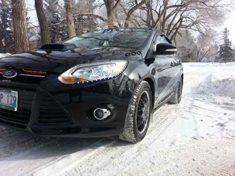 2012 Ford Focus - A black 2012 Ford Focus with a hood scoop is parked on a snowy road, with trees in the background.