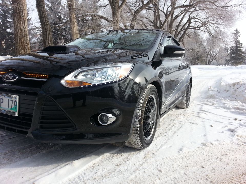 Black 2012 Ford Focus with hood scoop and LED accent lights on front grille, parked in snow