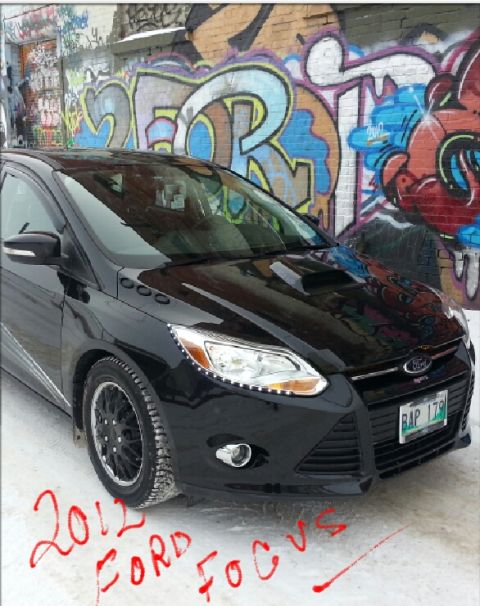 2012 Ford Focus - A black 2012 Ford Focus with custom hood scoop and aftermarket wheels is seen parked in front of a graffiti-covered wall.