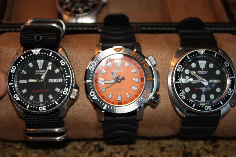 Three Seiko watches with black and orange faces and black straps, arranged side-by-side