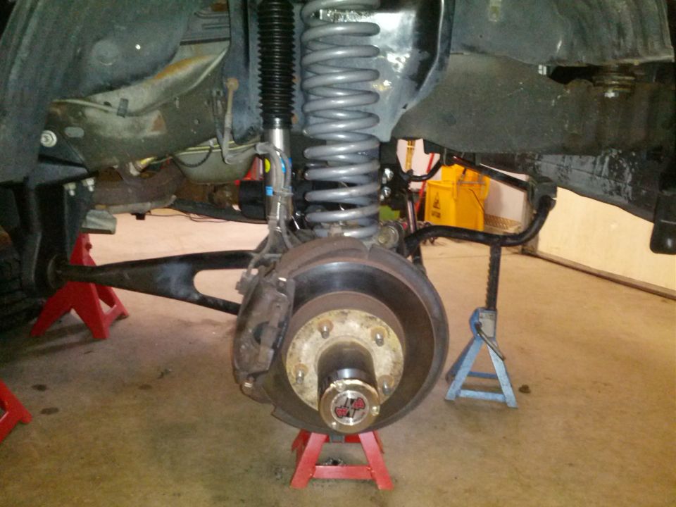Front wheel assembly of a 1995 Ford Bronco on jack stands, showing suspension components and brake rotor