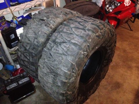 1990 Ford Bronco - Two large off-road tires are stored in a garage, with a red motorcycle in the background.