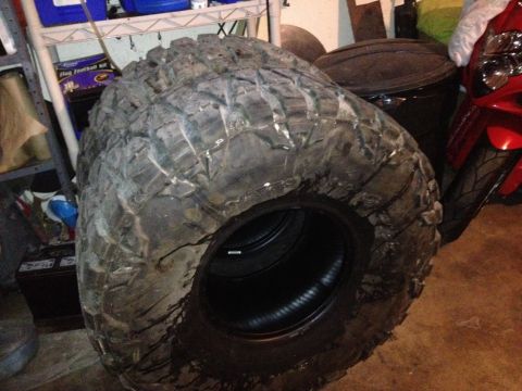 1990 Ford Bronco - A pair of aggressive off-road tires are stored indoors, with a motorcycle nearby.