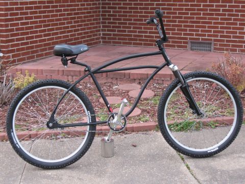 1994 Ford Bronco - A black cruiser bicycle is parked outside a brick building, wide tires and a unique pedal setup.