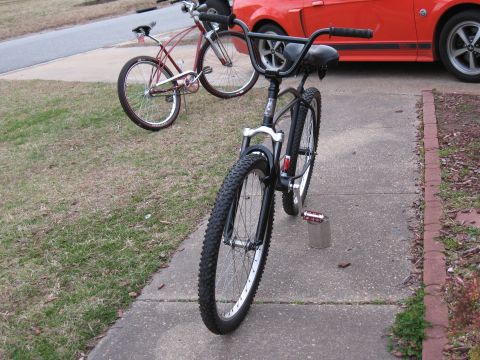1994 Ford Bronco - A red car is parked behind two bicycles on a sidewalk.