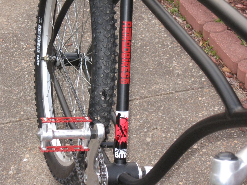 Black bicycle frame with red pedals, knobby tire, and "RATRODBIKES" text