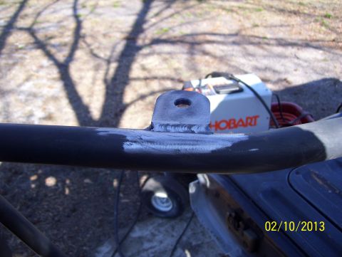 1990 Ford Bronco - A close-up view of a welding bracket attached to a dark metal tube, with a Hobart welder visible in the background.