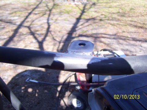 1990 Ford Bronco - A close-up view of a metal bracket with a hole, with a red and white object visible in the background.
