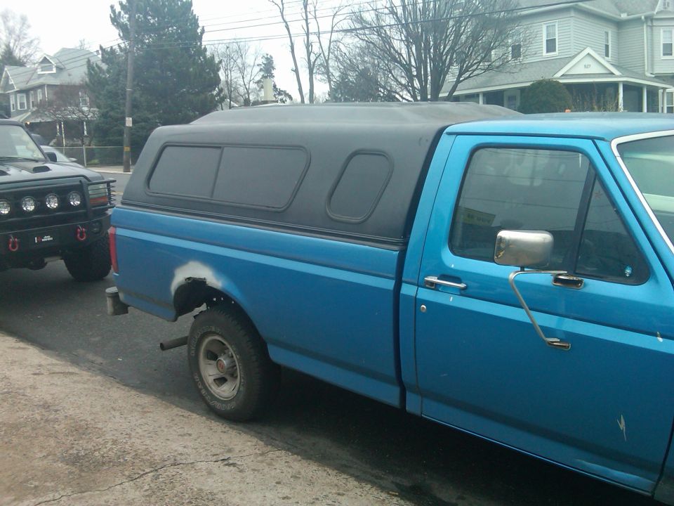 blue pickup truck with black camper shell parked next to a black SUV