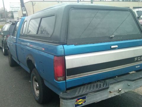 1993 Ford Bronco - Blue Ford pickup truck with a camper shell is parked next to another vehicle.
